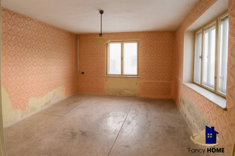 A room in a family house with peeling wallpaper on the walls and large windows.