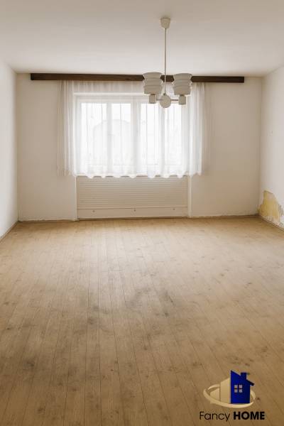 An empty room in a family house with a wood-decor floor and a large window with a curtain.