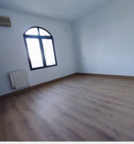 An empty room with an arched window, wood-patterned flooring, air conditioning, radiator.
