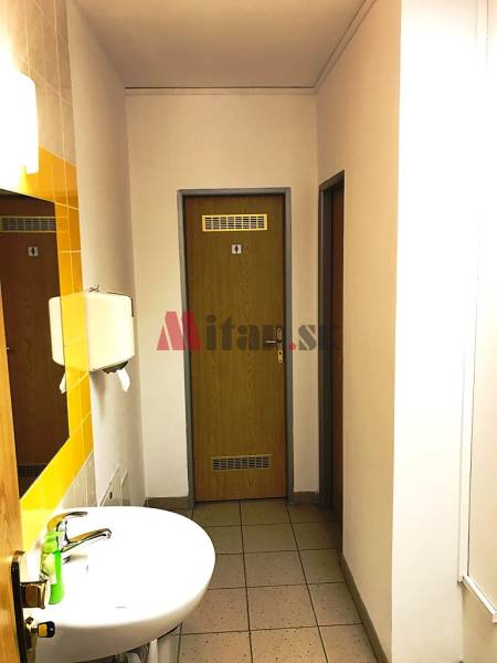 Office bathroom with a sink, mirror, and door with a symbol on the wall.