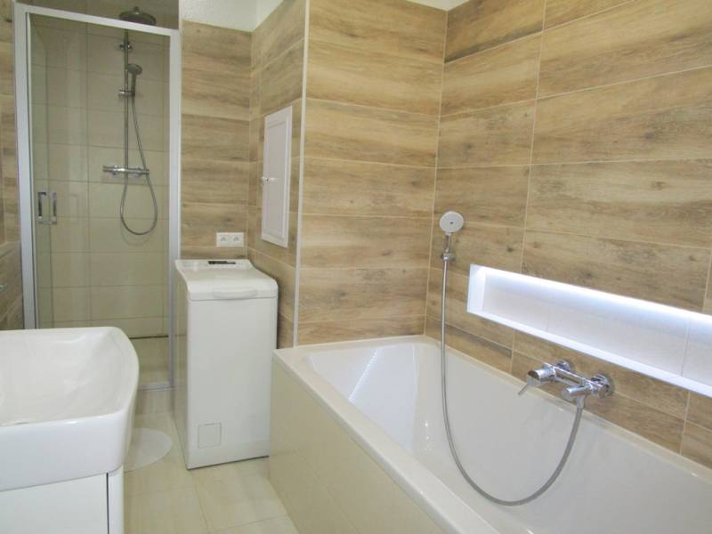 Bathroom with a bathtub, washing machine, and shower in a 2-room apartment. Wooden decor on the walls.