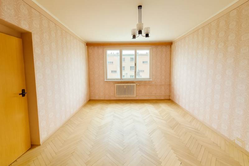 A room in a 2-room apartment with a wooden decor floor and wallpaper.