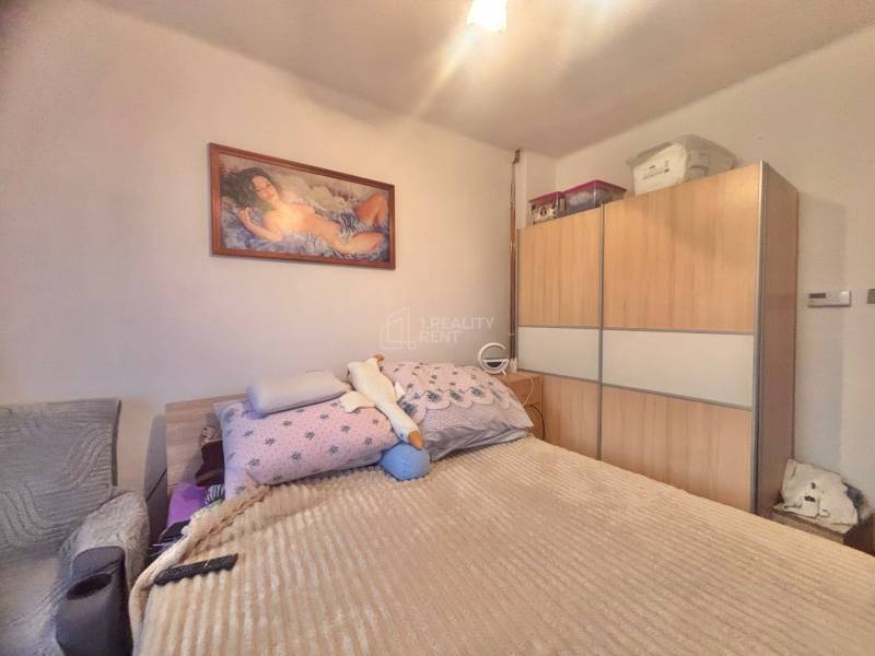 Bedroom in a family house with a painting above the bed, a large wardrobe, and a simple chair.
