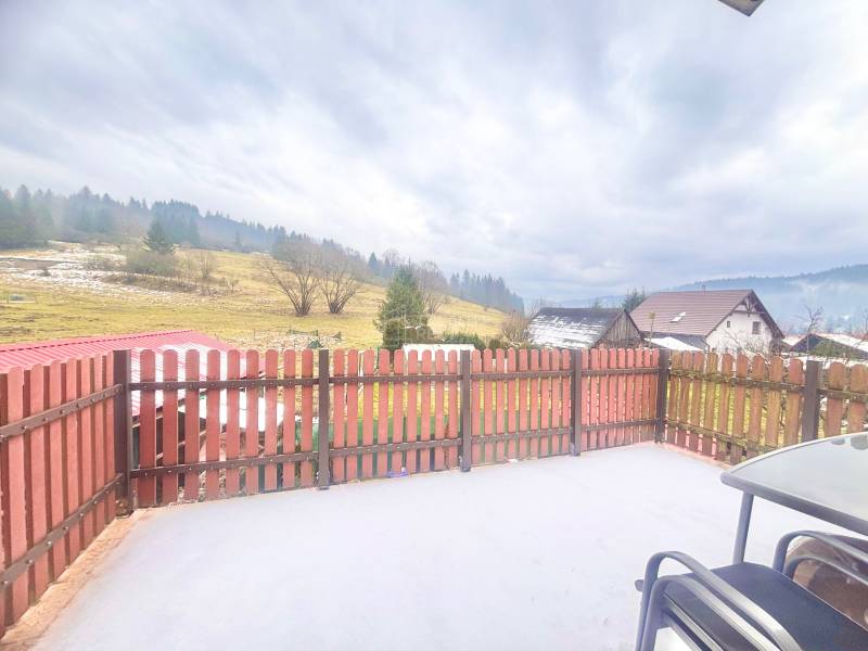 The courtyard of a family house in Predmier in Turzovka with a view of the hilly landscape and a fence.