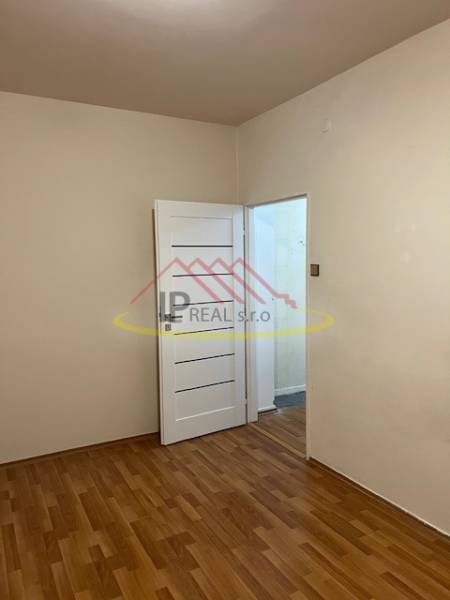 A room in a 2-room apartment with a wooden decor floor and closed white doors.
