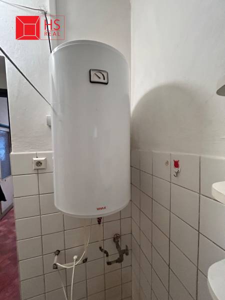 An electric boiler in the bathroom of a family house, covered with white ceramic tiles.