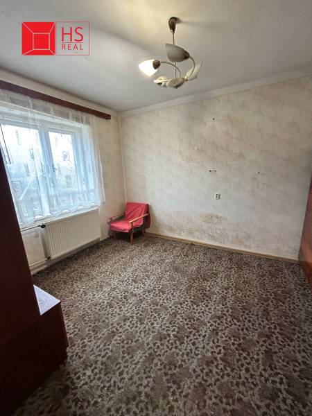 A room in a family house with a carpeted floor, a simple armchair, and curtains.