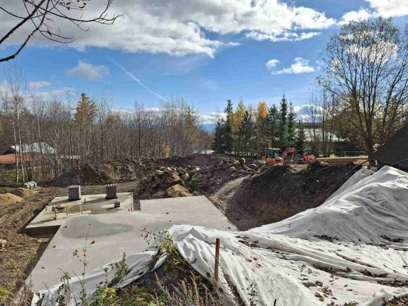 A construction site in Starý Smokovec for the development of a recreational apartment surrounded by trees and building materials.