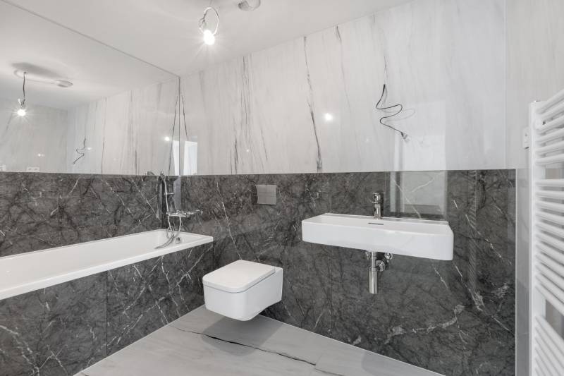 A bathroom with marble tiles, a bathtub, a sink, and a wall-mounted toilet in a 3-room apartment.
