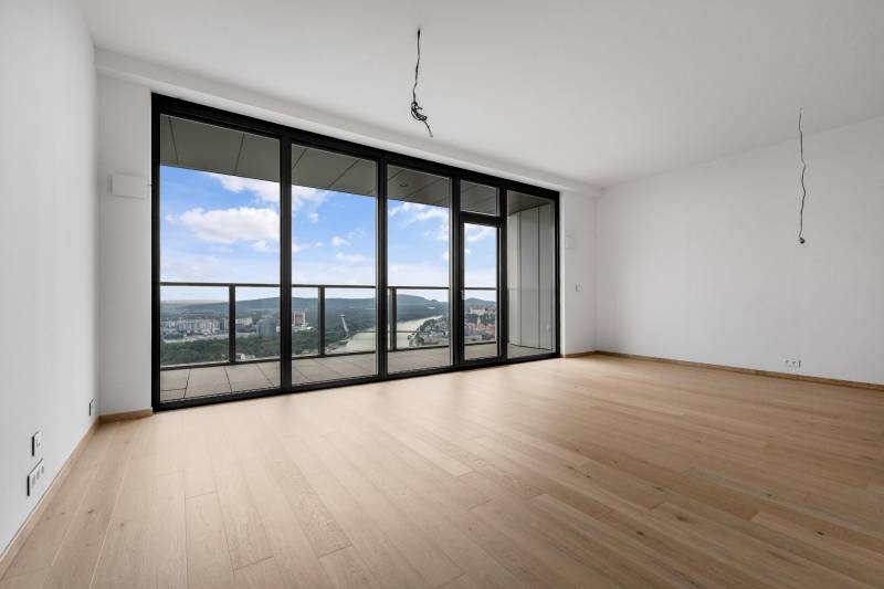 A spacious living area with large windows and wood-patterned flooring in a 3-room apartment.