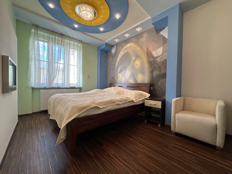 A bedroom in a two-room apartment with a wooden decor floor and an artistic wall.