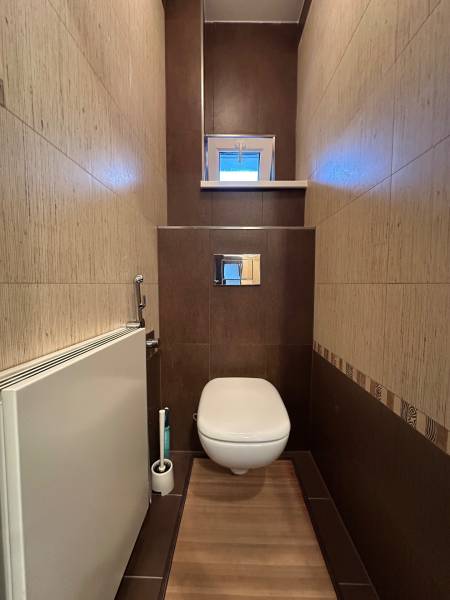 A toilet with brown-toned tiles and a floor with a wood decor in a 2-room apartment.
