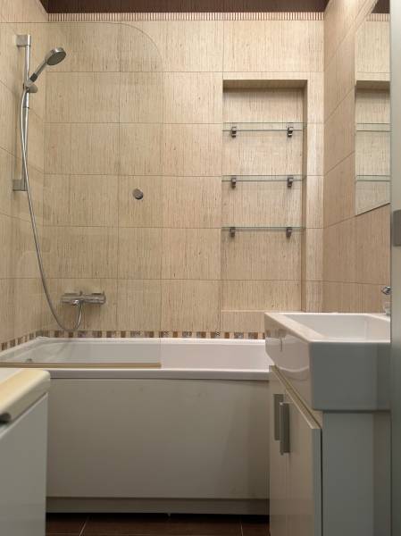Bathroom with a bathtub and shower in a 2-room apartment with ceramic tiles.