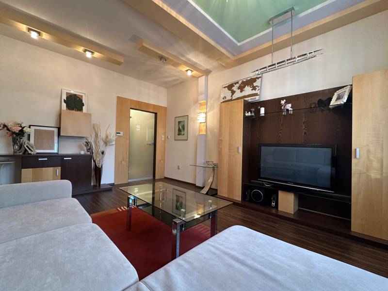 Living room in a two-room apartment with a sofa, glass table, and television, floor with wood decor.