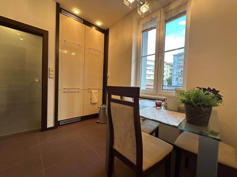 Dining area in a 2-room apartment with a large window and a table with square chairs.