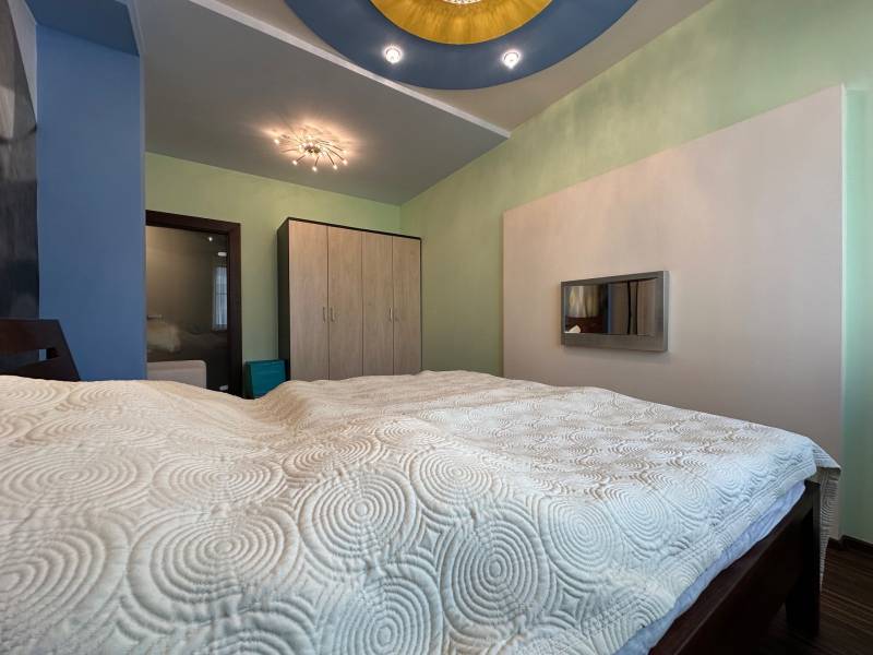 A bedroom with a wood-patterned floor, light-colored furniture, and interesting ceiling lighting.