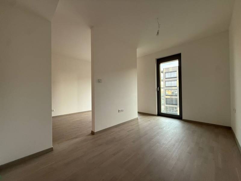 A room in a 2-room apartment with a wooden decor floor and balcony doors.