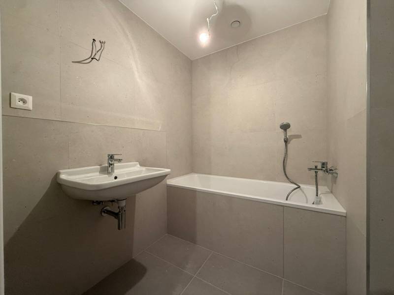 Bathroom in a 2-room apartment, light tiles, bathtub, sink, simple furnishings.