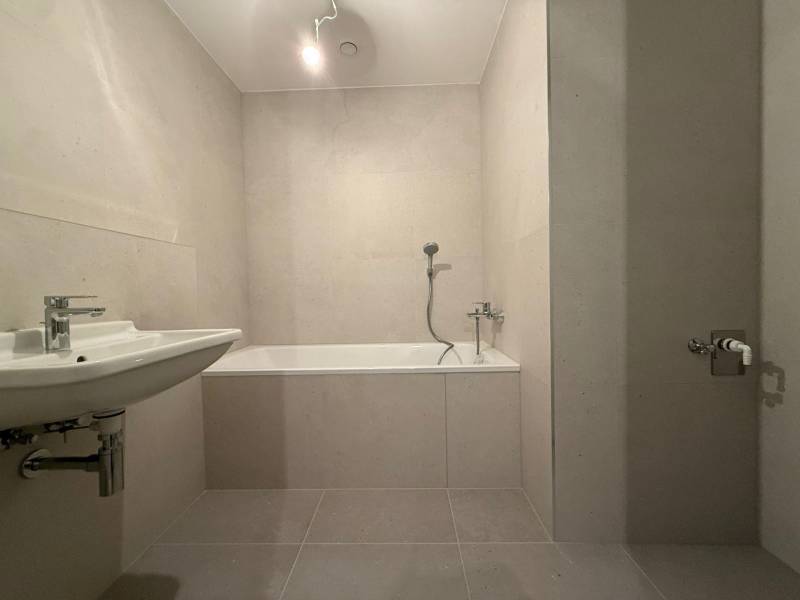 A bathroom in a 2-room apartment with a bathtub, sink, and neutral tiles.