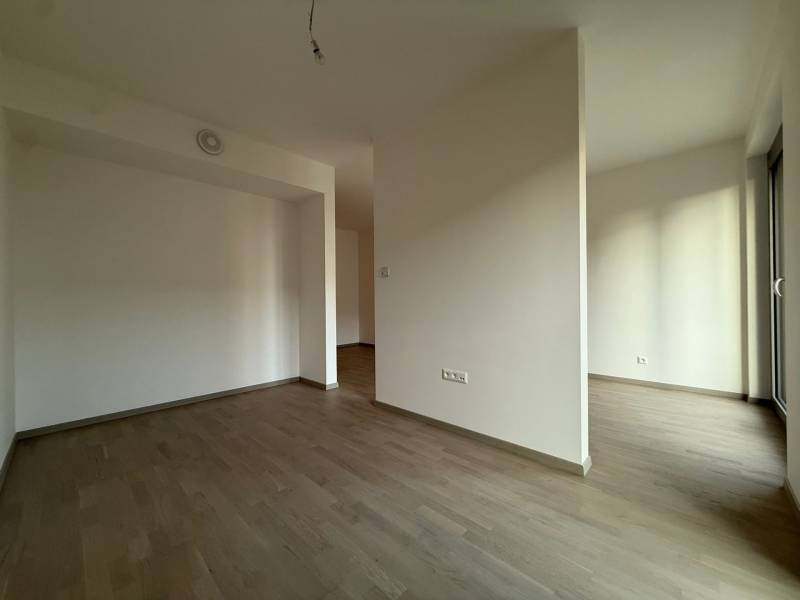 An empty room in a 2-room apartment with wood-patterned flooring and white walls.