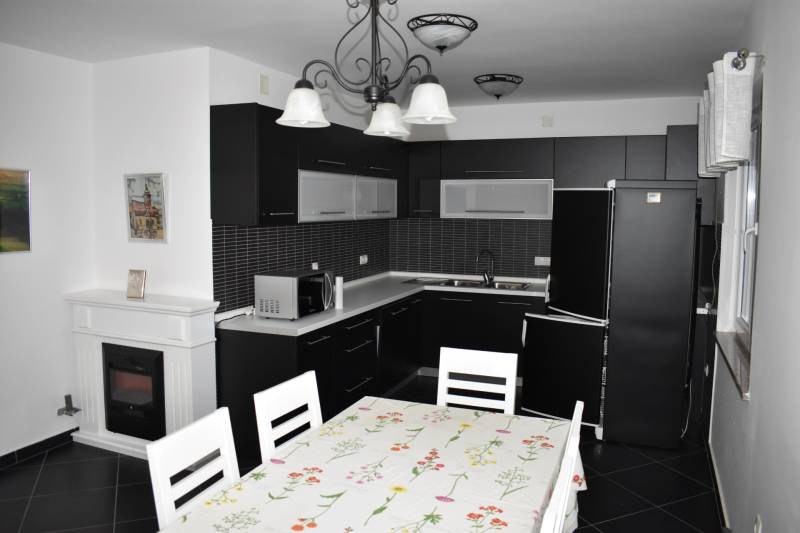 A kitchen with black furniture, a dining table, and a white fireplace in a family house.