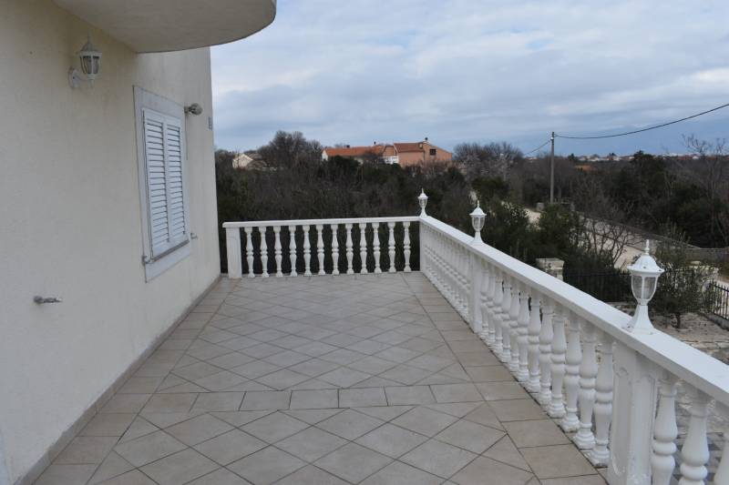 The terrace of a family house in Pridraga with white railings and lights, overlooking the landscape.