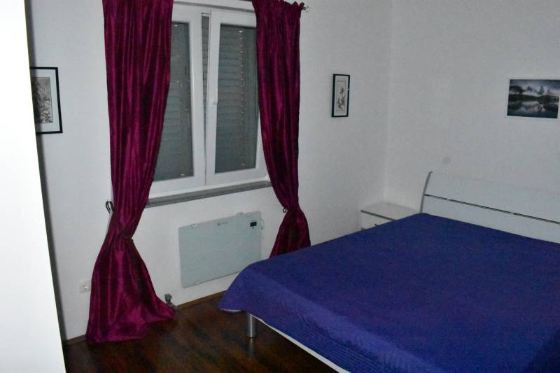 Bedroom with purple curtains, a blue bedspread, and a wood-patterned floor in a family house.