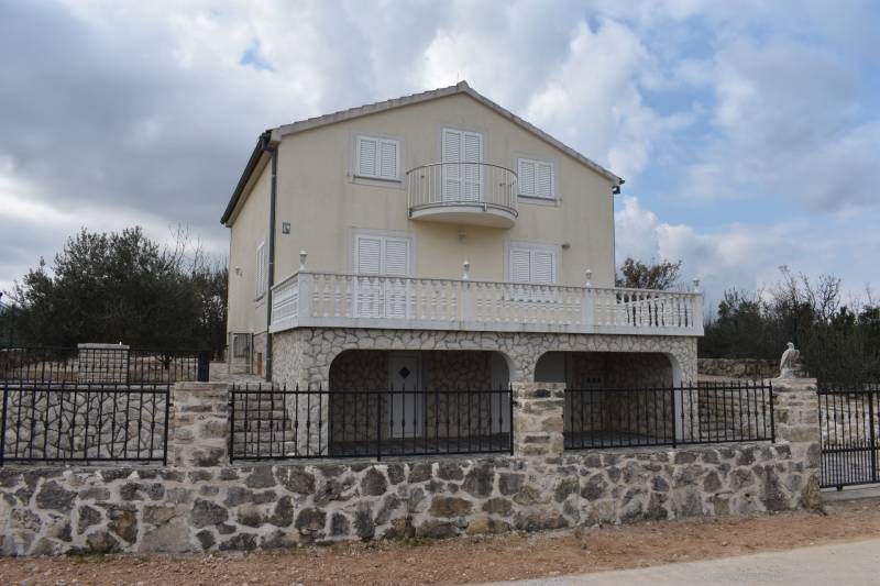 A family house in Pridraga with a stone facade and a balcony, surrounded by a stone fence.