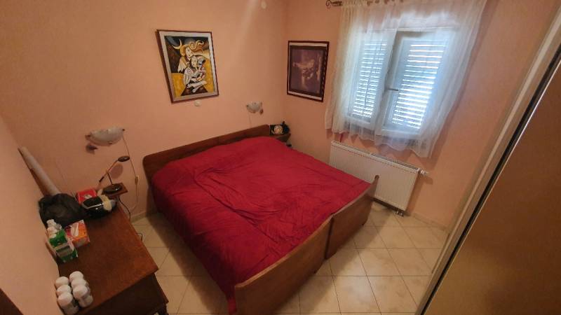 Bedroom in a family house with a double bed, colorful paintings, and light tiles.