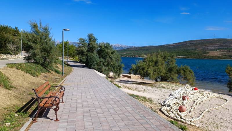 Coastal road in Pridraga with a bench, greenery, and a view of the sea.