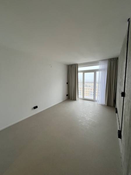 Studio apartment with large windows, light curtains, and light flooring with a view of the city.