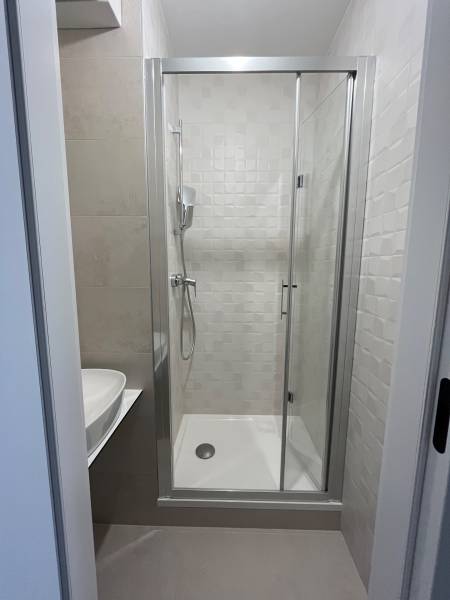 A shower corner with a sink in a studio apartment, with light tiles.