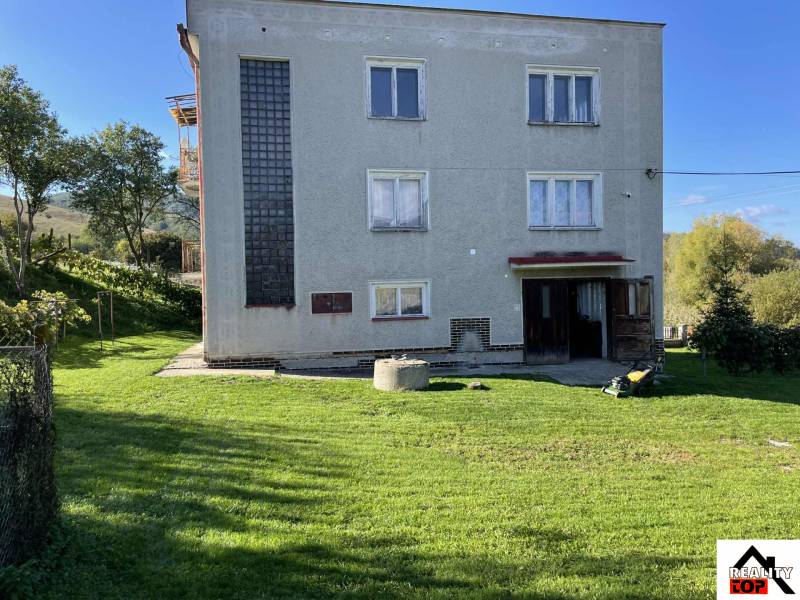 A family house in Hajnáčka with a lawn, trees, and garden tools in the yard.