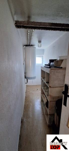 A narrow interior of a family house with a boiler and shelves, light walls, and a floor with a wooden decor.
