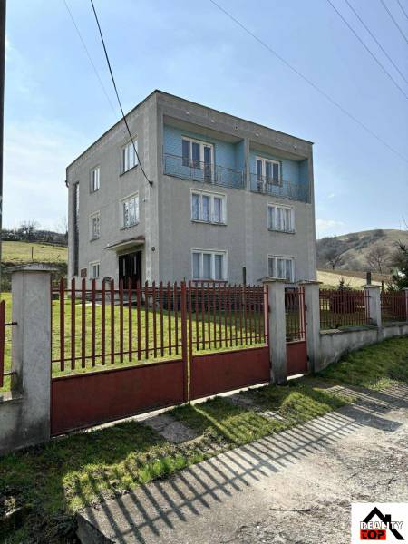 A family house in Hajnáčka with three floors, a red gate and fencing in front of it.