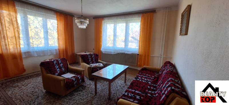 A living room in a family house with orange curtains, a sofa, and a coffee table.