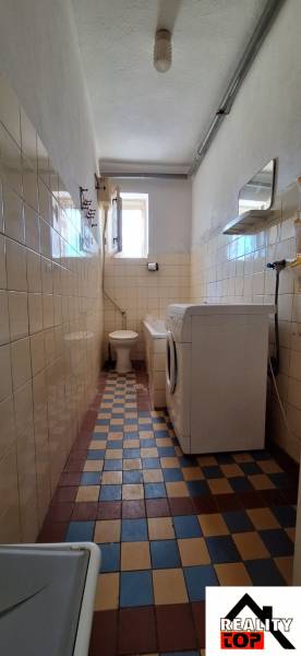 A narrow bathroom in a family house with a toilet, tiles, and a washing machine.