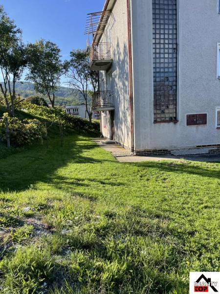 A family house in Hajnáčka with a grassy plot, trees, and balconies on a sunny day.