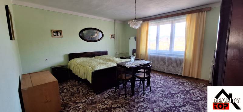 Bedroom in a family house with carpets, a bed, and a large window with curtains.