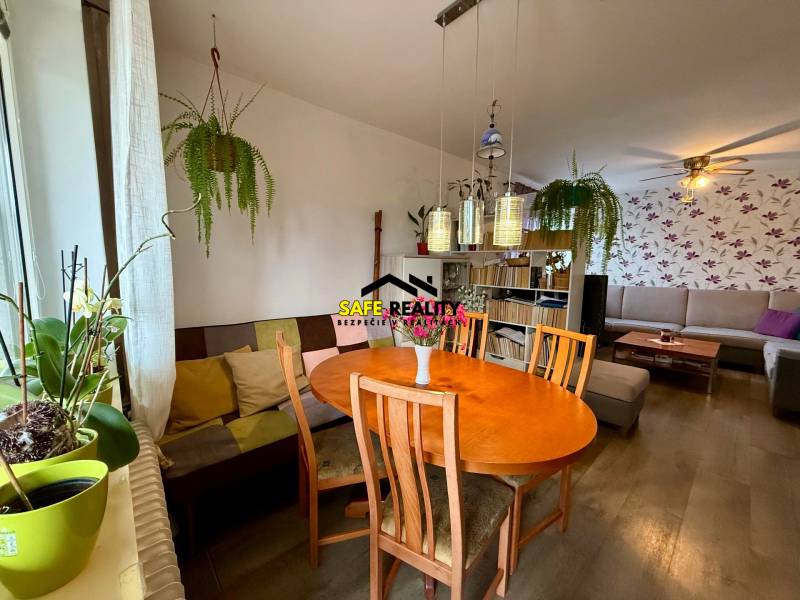 Living room with a dining table, wood-patterned floor, plants, and a colorful sofa.