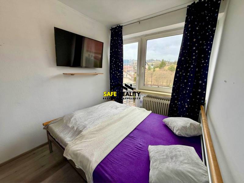 A bedroom in a family house with a television and a view through the window, floor with wooden decor.