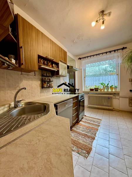 A kitchen in a family house with a view of the garden, light tiles, wooden cabinet decor.