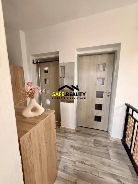 A hallway in a family house with light doors, a floor with a wood decor, and a decorative vase.