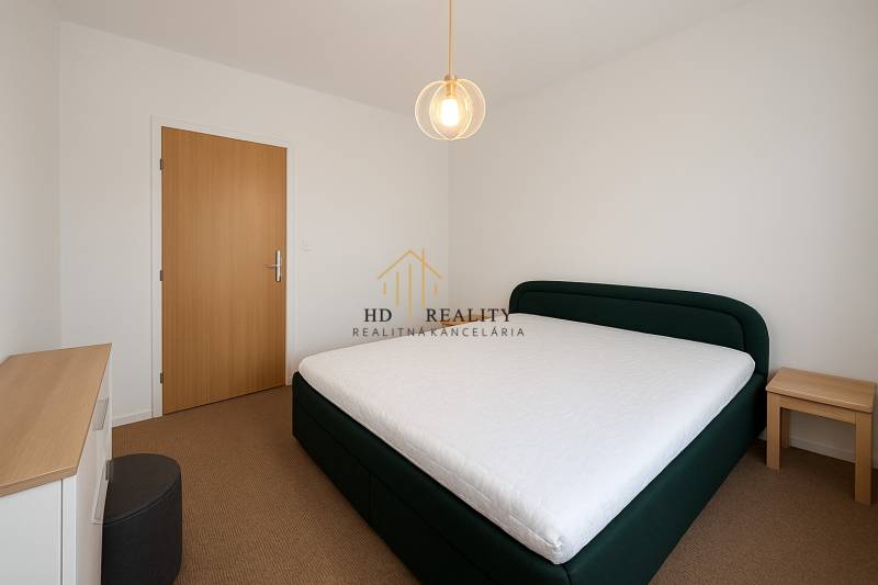 Bedroom in a 3-room apartment with a bed and a chair, white wall and wooden door.
