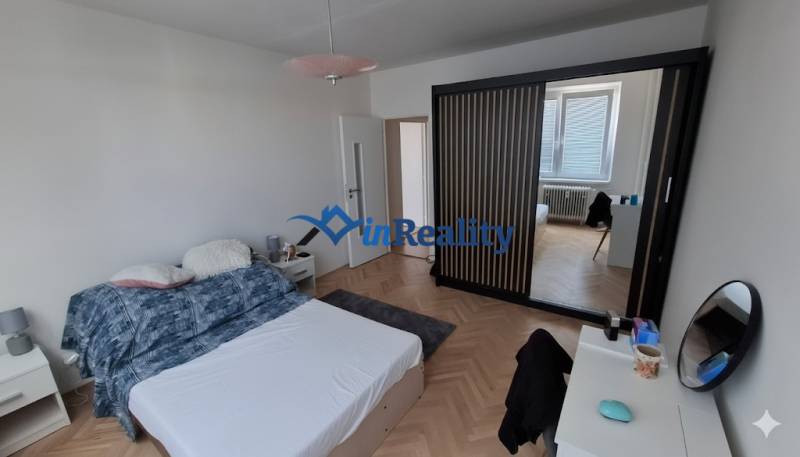 A bedroom in a three-room apartment with a wood-patterned floor and a built-in wardrobe.