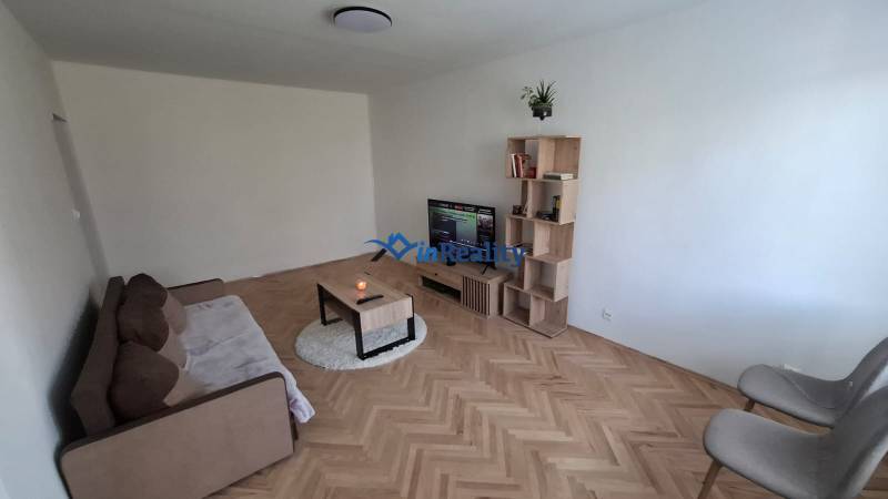 Living room in a 3-room apartment with a sofa, TV, and wooden decor flooring.
