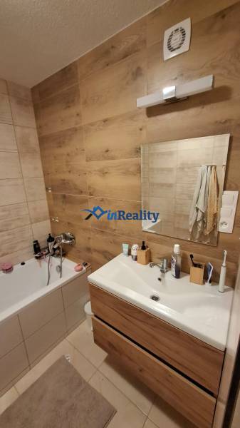 A bathroom with wooden floor decor, a bathtub, and a sink in a 3-room apartment.