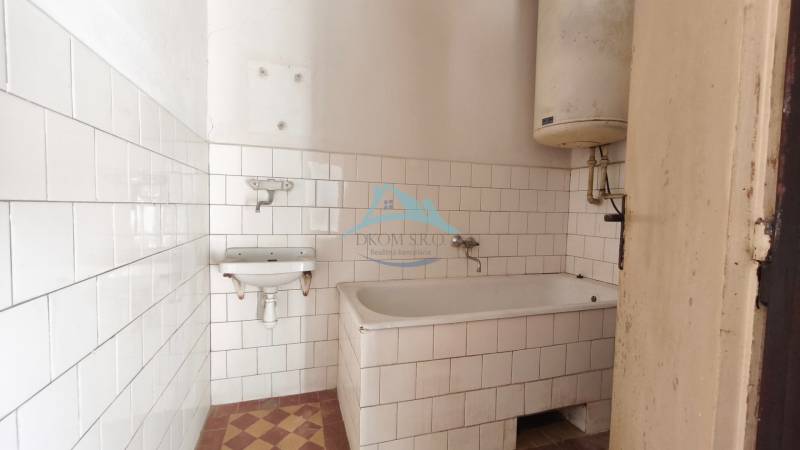 A bathroom in a family house with a bathtub, white tiles, and a water heater.