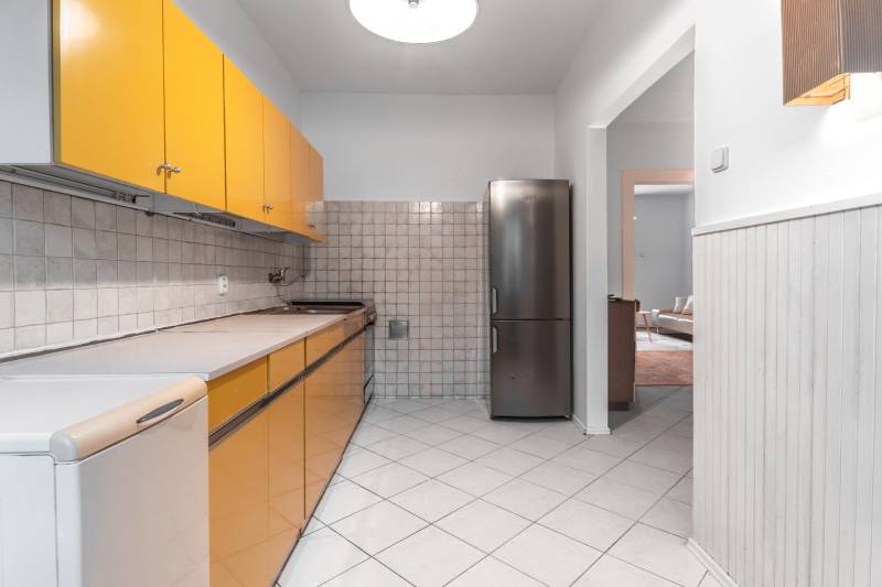 A kitchen in a 3-room apartment with tiles, yellow cabinets, and a stainless steel refrigerator.