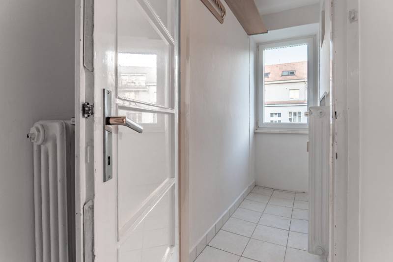 A narrow room with a window, tiled floor, and a white radiator in a 3-room apartment.
